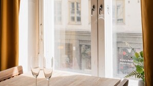 Ein Zimmer mit Holztisch, zwei Weingläsern und Blick auf ein Gebäude durch eine Glastür.