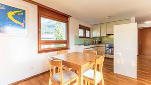 A modern kitchen with wooden cabinets, a dining table with chairs, and a window with a view of a mountain.