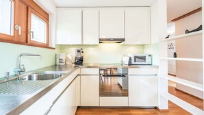 A modern kitchen with white cabinets, stainless steel appliances, and wooden flooring.