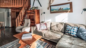 A living room with a leather sofa, a wooden coffee table, a patterned cushion, a painting, and a mounted animal hide.