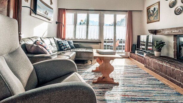 A living room with a sofa, a coffee table, a fireplace, and a view through the windows.