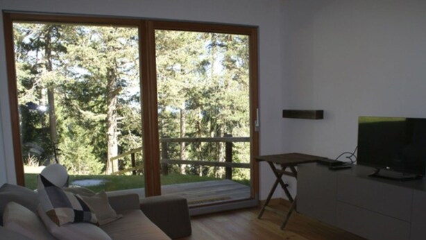 Un salón moderno con un sofá, televisión y vistas a árboles a través de una puerta corrediza de vidrio.
