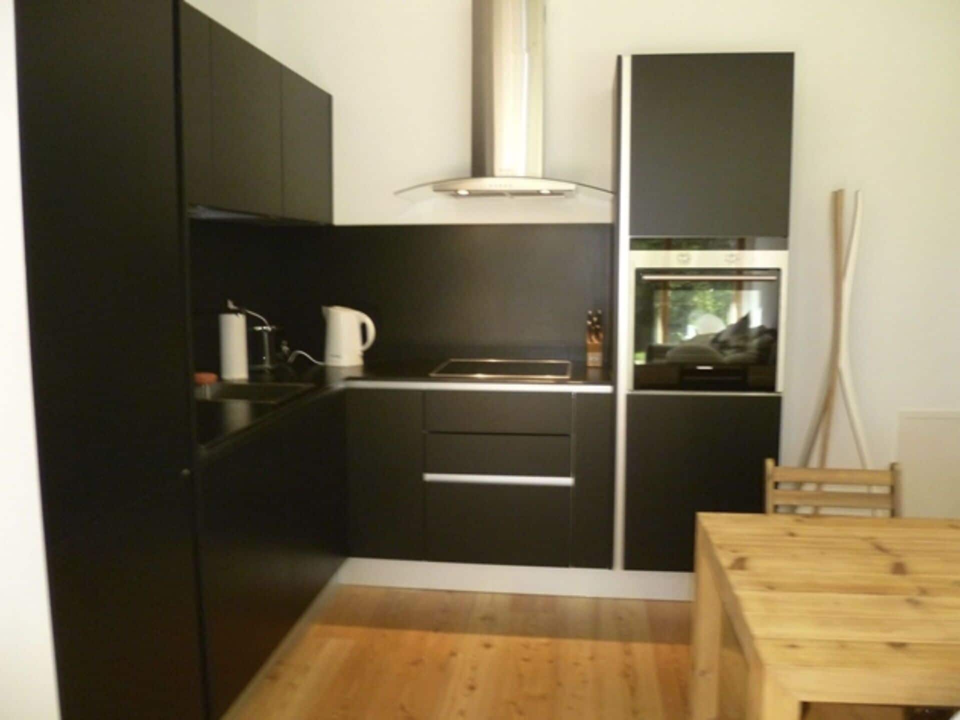 A compact kitchen with dark cabinetry, a wooden dining table, and a window.
