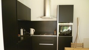 Cocina compacta con armarios oscuros, una mesa de comedor de madera y un ventanal.