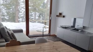 Un interior moderno con una mesa de comedor de madera, un sofá y una zona de cocina con armarios blancos y un gran ventanal.