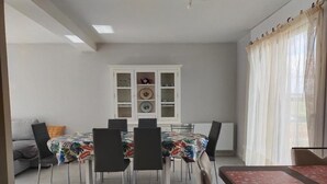 A dining area with a table and chairs, a cabinet with glass doors, and a window with curtains. - New 3-bedroom bungalow (Mouzeil)