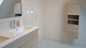 A modern bathroom with a large mirror, a sink, and a shower area. - New 3-bedroom bungalow (Mouzeil)