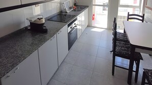 Moderni keittiö, jossa on valkoiset kaapit, graniittitaso sekä ruokailutila, jossa on pöytä ja tuolit.