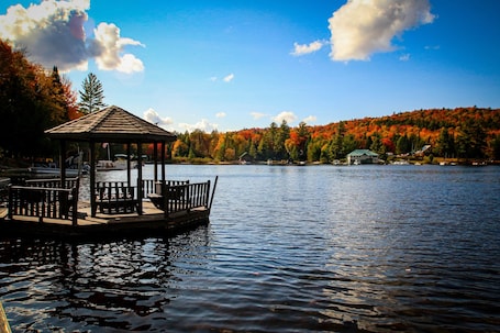 A wooden gazebo with benches on a lake, surrounded by autumn-colored trees and a clear sky.. Deer Run - Big Moose Lakeside
