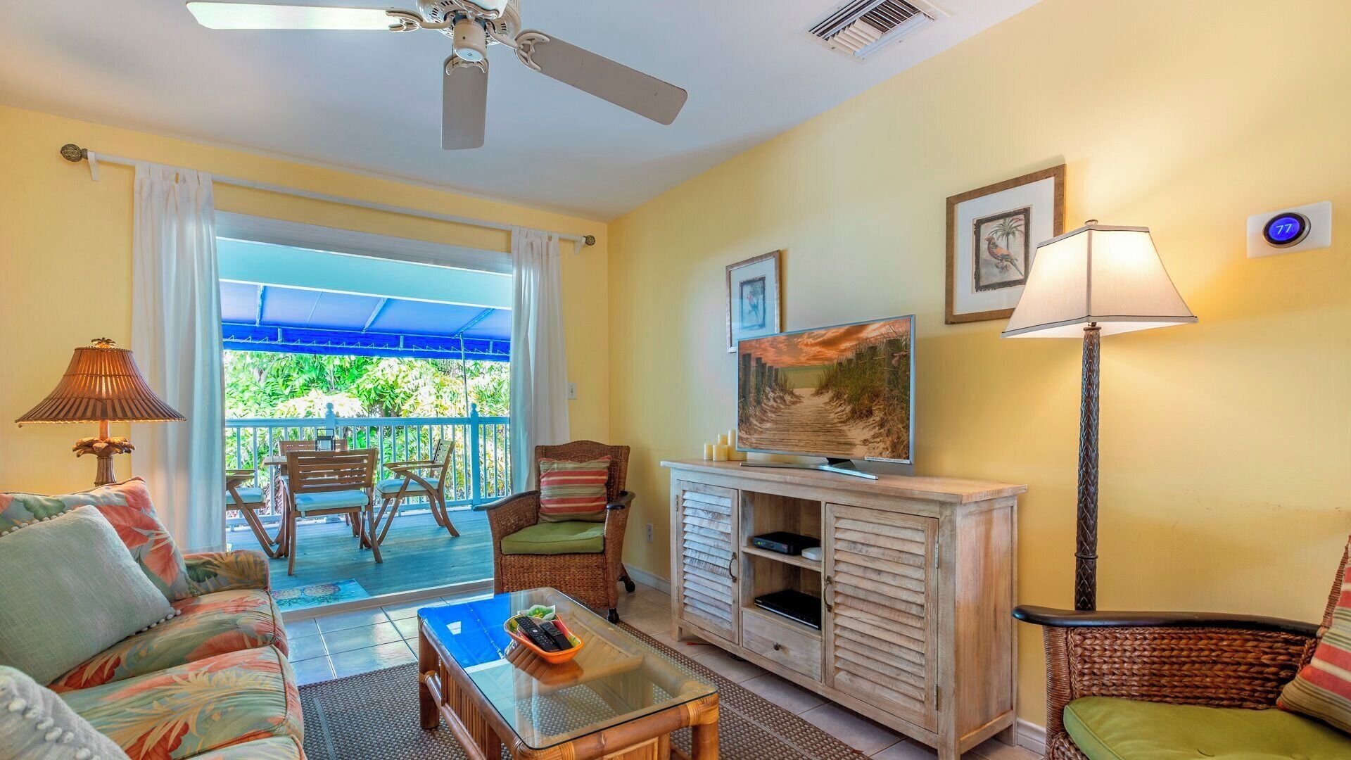 A room with a ceiling fan, a television, a sofa, a coffee table, and a balcony with outdoor furniture.