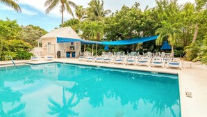 Ein Swimmingpool mit Liegestühlen und einer schattigen Liegefläche, umgeben von Palmen und viel Grün.