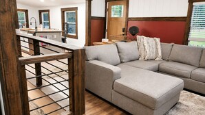 Ein modernes Wohnzimmer mit Ecksofa, Holzboden und einer Treppe, die in ein Obergeschoss führt.