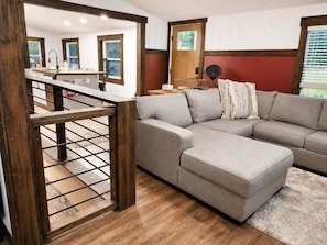 A modern living room with a sectional sofa, wooden flooring, and a staircase leading to an upper level.