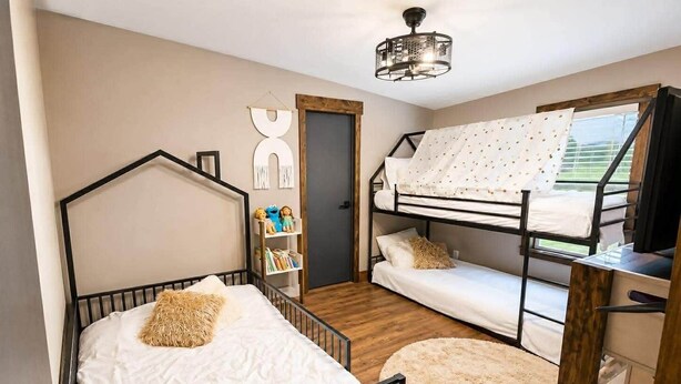 Ein Schlafzimmer mit einem Etagenbett, einem Einzelbett, Holzboden, einem Bücherregal und einem Fenster mit Vorhängen.