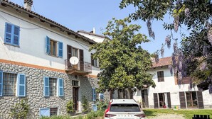 Une voiture blanche est garée devant un bâtiment en pierre, doté de volets bleus et d’un balcon.