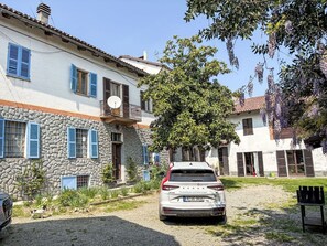 A white car parked in front of a stone building with blue shutters and a balcony.