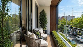 Een balkon met rieten meubels, een plant in pot en uitzicht op een straat.