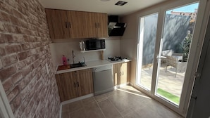 A compact kitchen with wooden cabinets, a microwave, a dishwasher, and a sliding glass door leading to an outdoor area. - La dorée, a private room in an independent apartment (Billère)
