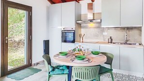 Una cocina con armarios blancos, horno empotrado y comedor con una mesa redonda y sillas.