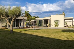 Eine moderne Villa mit großzügiger Rasenfläche, Außenmöbeln und freiem Blick zum Himmel.