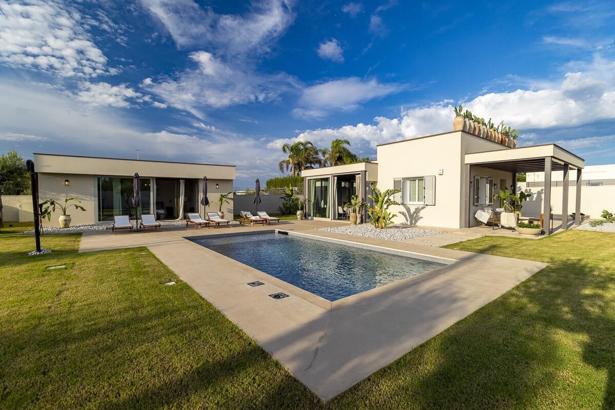 Een modern huis met een zwembad, twee aparte gebouwen en een verzorgd gazon.