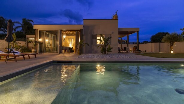Una casa moderna con piscina, area salotto esterna e ingresso ben illuminato.