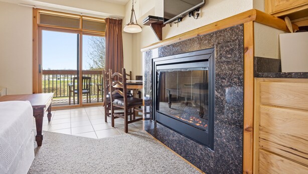 A room with a fireplace, a dining table with chairs, a TV mounted on the wall, and a sliding glass door leading to an outdoor area. - Chula Vista Resort Studio Villa in Wisconsin Dells! Free Waterpark Passes! (Wisconsin Dells)