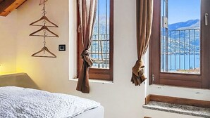 Een slaapkamer met een bed, een houten plafond, een raam met gordijnen en uitzicht op bergen.
