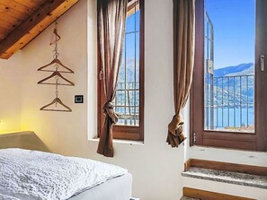 Ein Schlafzimmer mit einem Bett, einer Holzbalkendecke, einem Fenster mit Vorhängen und Blick auf Berge.