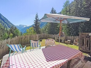 En uteplats med ett bord och stolar, ett trästaket och utsikt över bergen.