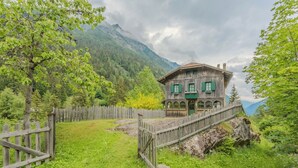 Ein rustikales Holzhaus mit einer Holzbrücke, umgeben von üppigem Grün und Bergen.