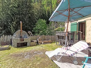 En trädgård med en stenugn, ett trästaket och en möblerad uteplats med bord och stolar.