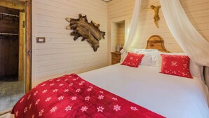 Ein Schlafzimmer mit Holzboden, einem Himmelsbett, einem an der Wand befestigten Tierfell und einer Holztür.