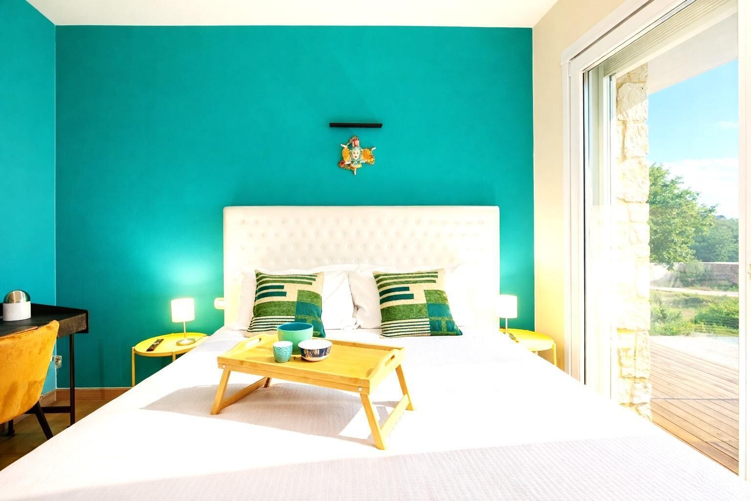 Camera da letto con una parete verde acqua, un letto bianco e vista sull'esterno.