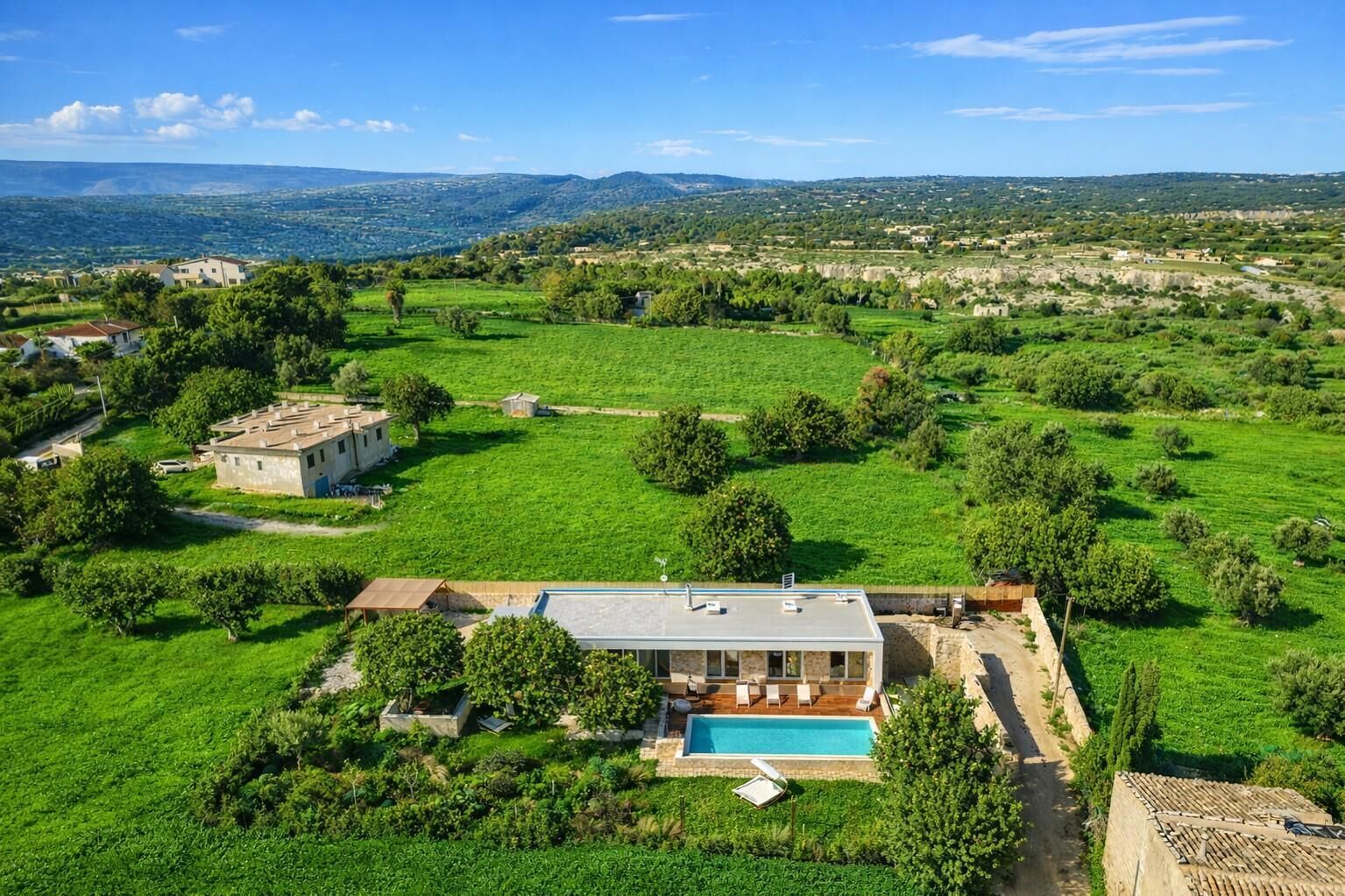 Una casa moderna con piscina, immersa in prati verdi e circondata da montagne lontane.