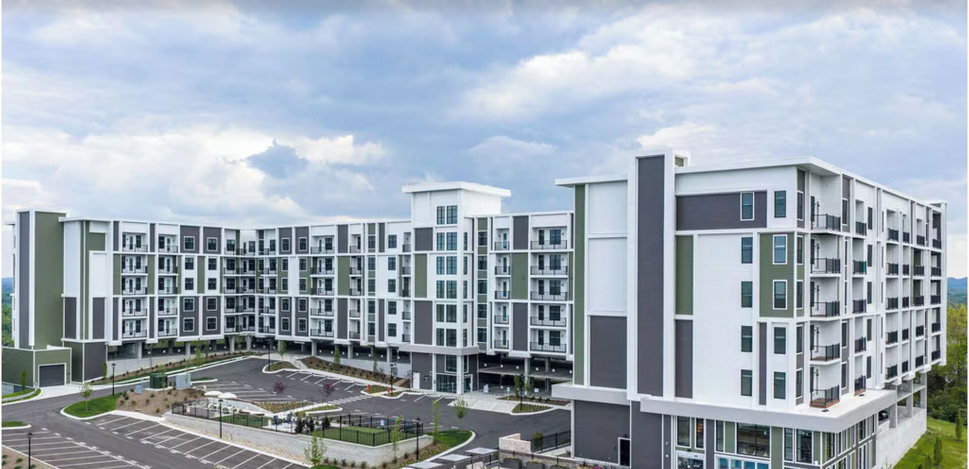 A multi-story residential building with a central courtyard, balconies, and a parking area.