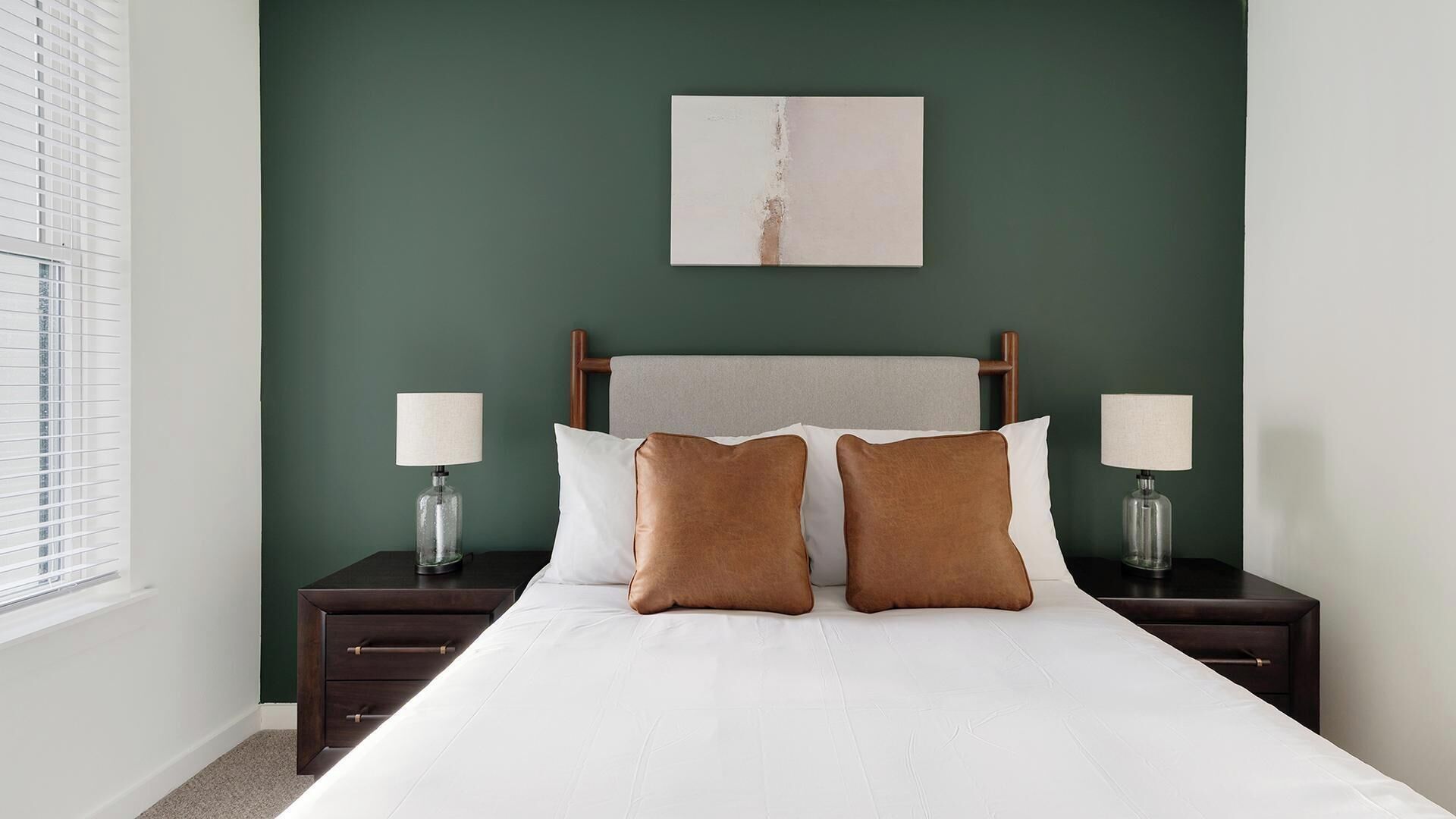 A neatly made bed with two pillows, a headboard, and two bedside tables with lamps.