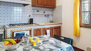 Une cuisine avec des carreaux décorés, des armoires en bois, une cuisinière à gaz et une table à manger agrémentée d’un panier de fruits et de tasses.