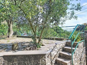Eine steile Steintreppe führt zu einem grünen Metallgeländer, umgeben von Olivenbäumen und einer Steinmauer.
