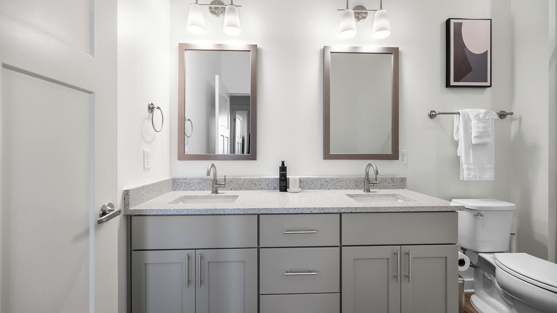 A modern bathroom with two sinks, a toilet, and a towel rack.