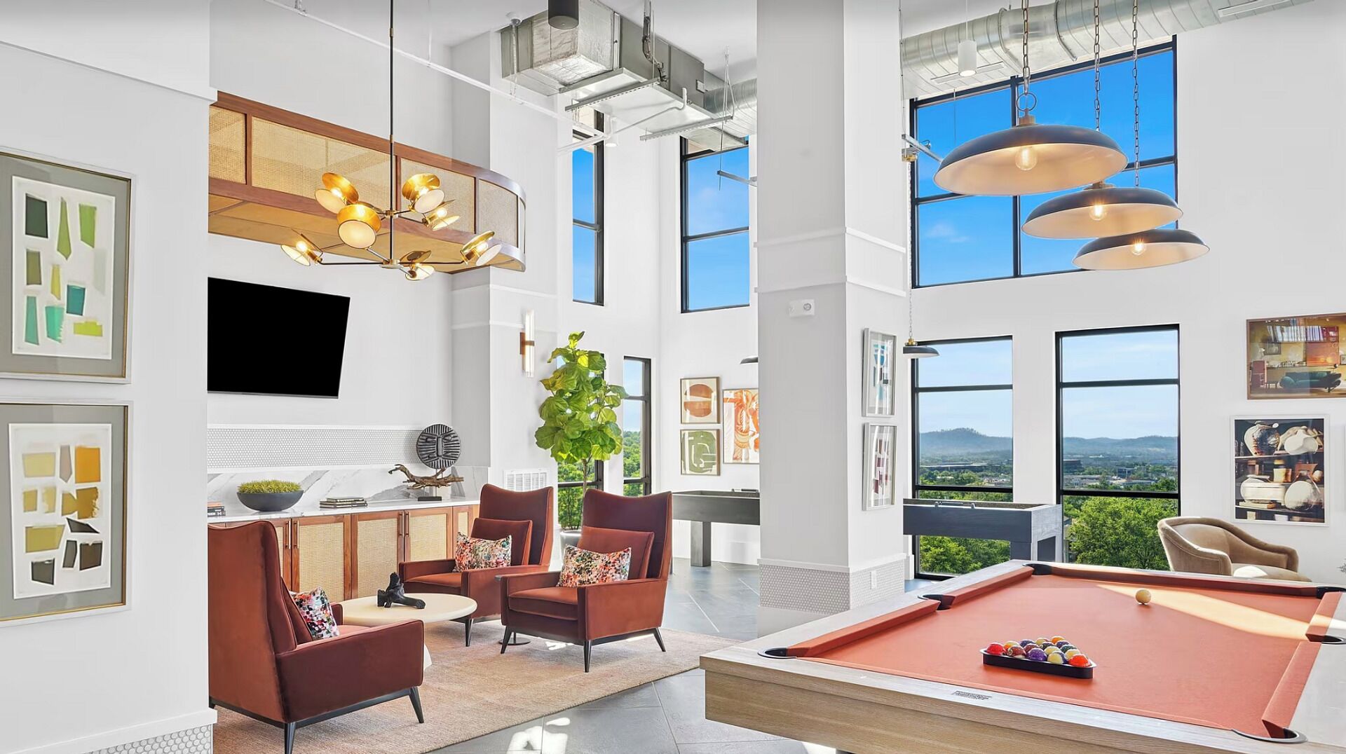 A spacious room with a pool table, comfortable seating, large windows, and a modern chandelier.