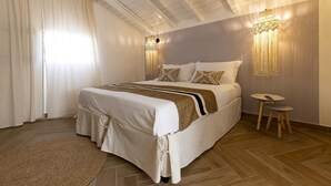 Un dormitorio con cama, cortinas, alfombra, lámpara de pared y una mesita.