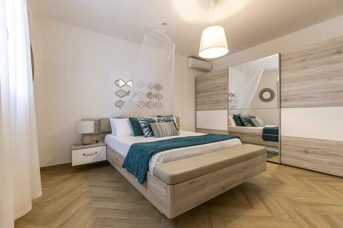 A bedroom with a bed, bedside table, lamp, mirror, and decorative wall art.