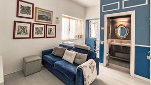 Ein Zimmer mit einem blauen Sofa, einem kleinen Tisch und gerahmten Kunstwerken an der Wand.