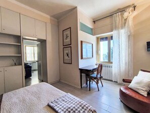 Una camera da letto con un letto, una scrivania, una sedia, un divano e una finestra con tende.