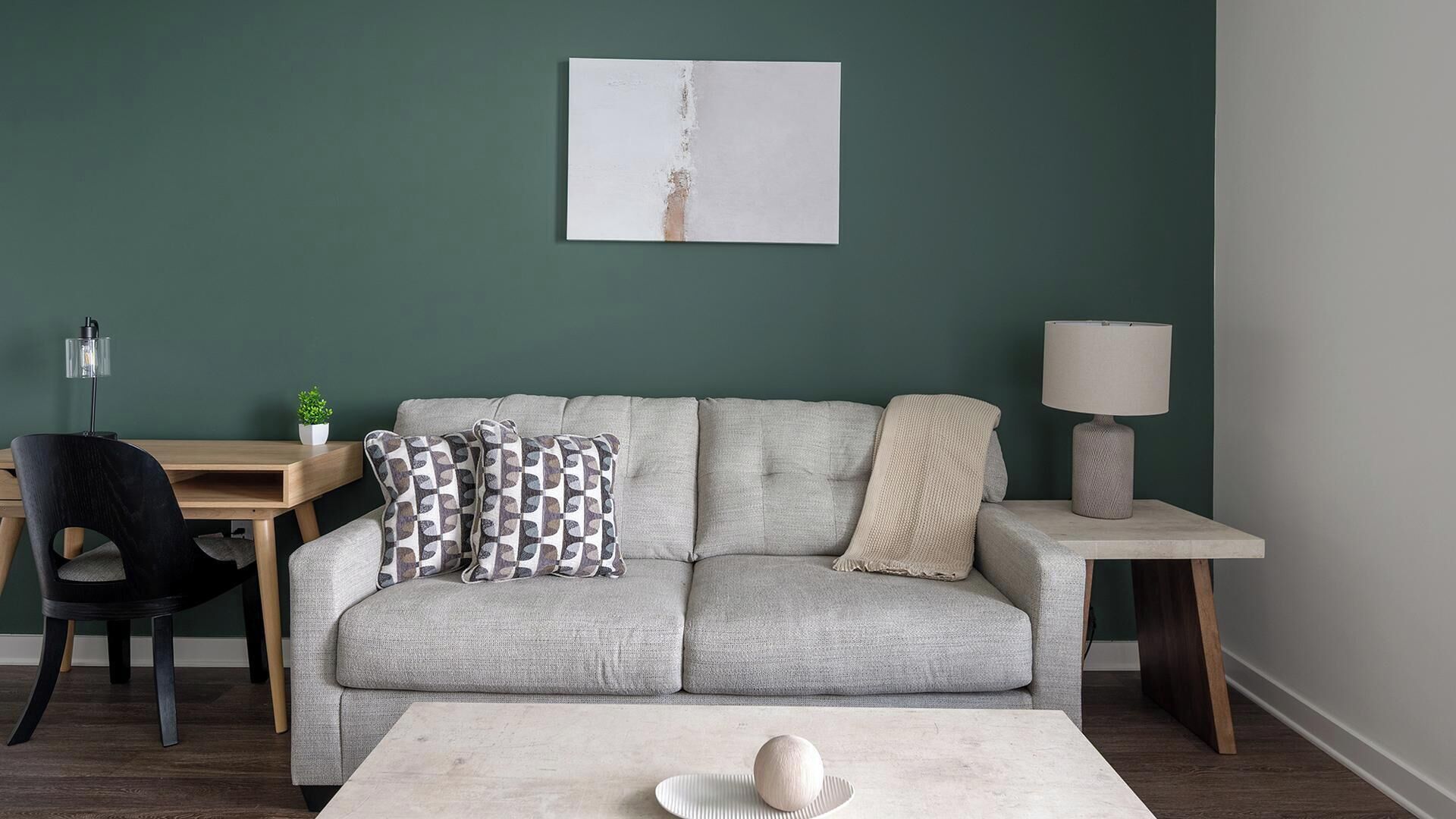 Una sala de estar con un sofá gris, una mesa de centro, una lámpara, un escritorio y una silla.