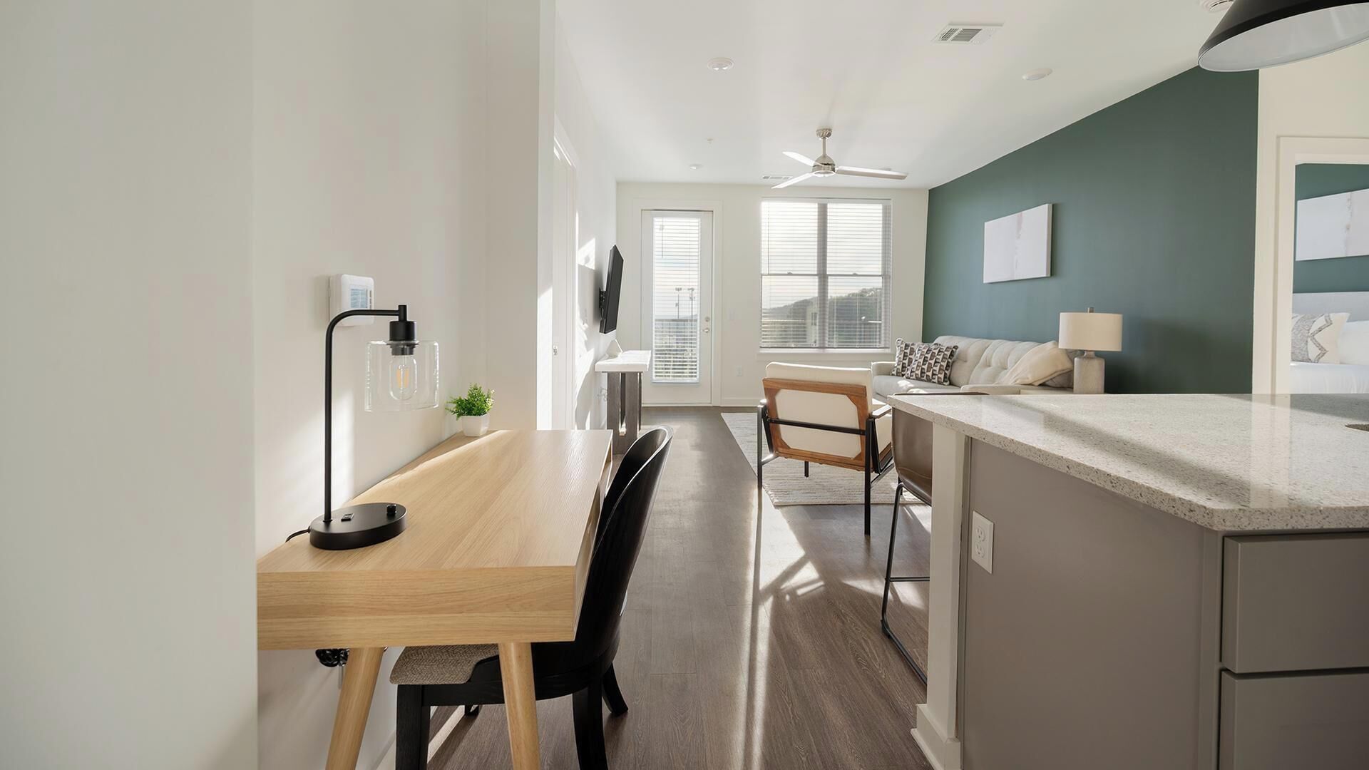 A modern kitchen with a wooden countertop, a dining area with a chair, a ceiling fan, and a window with blinds.