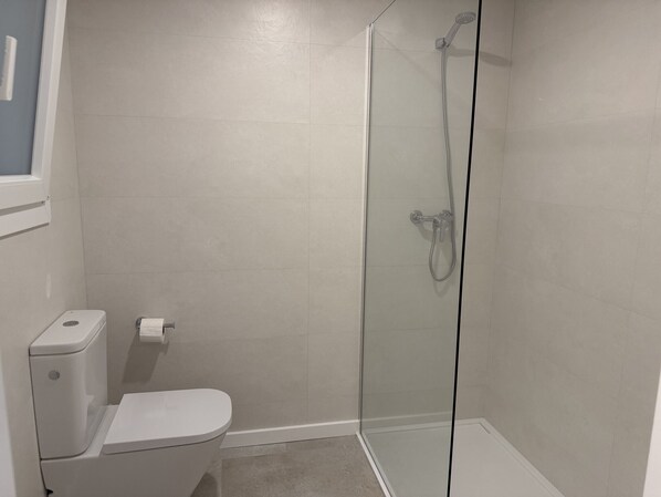 Une salle de bain avec des toilettes, une douche en verre et un mur blanc.