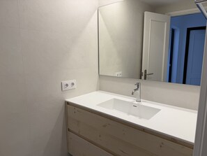 Une salle de bain avec un lavabo blanc, un meuble-lavabo en bois et un miroir. Il y a deux prises électriques sur le mur.
