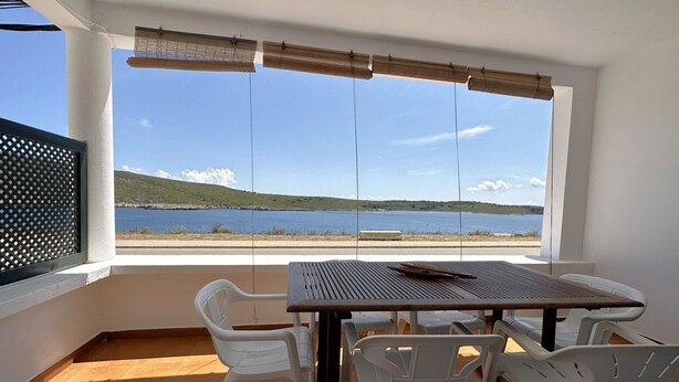 A balcony with a table and chairs, a view of a lake, and a white wall.